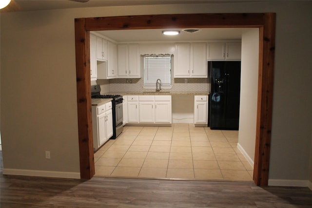 kitchen featuring backsplash, stainless steel gas range oven, black fridge with ice dispenser, sink, and white cabinets