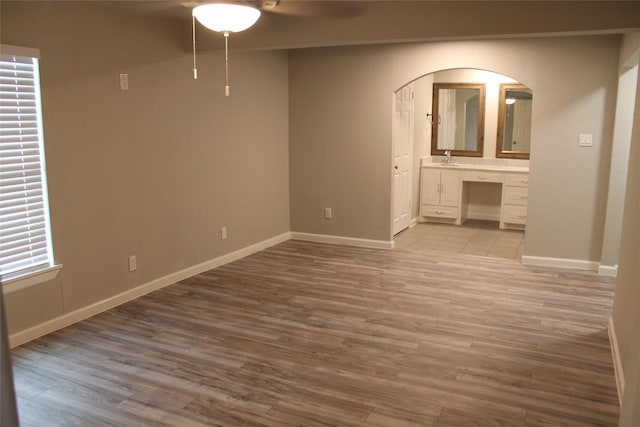 unfurnished bedroom featuring ceiling fan, light wood-type flooring, sink, and ensuite bath