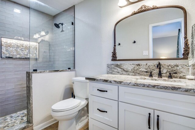 bathroom with a tile shower, vanity, and toilet