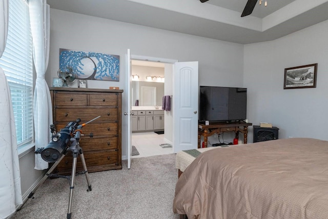 bedroom with a tray ceiling, ceiling fan, ensuite bathroom, and light colored carpet