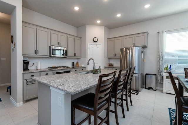 kitchen with light stone countertops, sink, a kitchen breakfast bar, a center island with sink, and appliances with stainless steel finishes