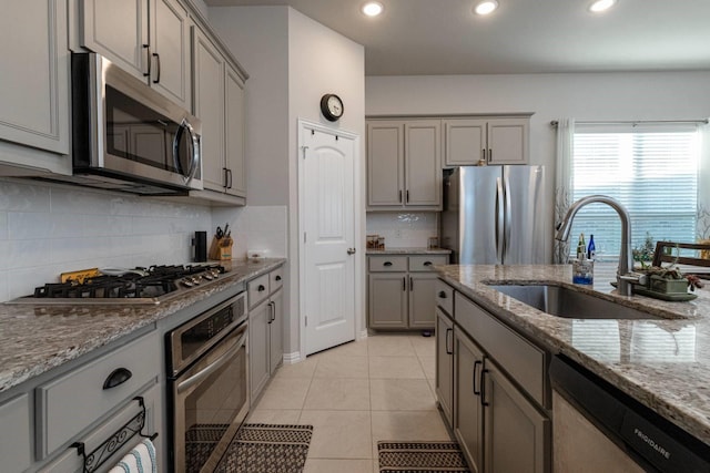 kitchen featuring gray cabinetry, sink, light tile patterned floors, appliances with stainless steel finishes, and light stone counters