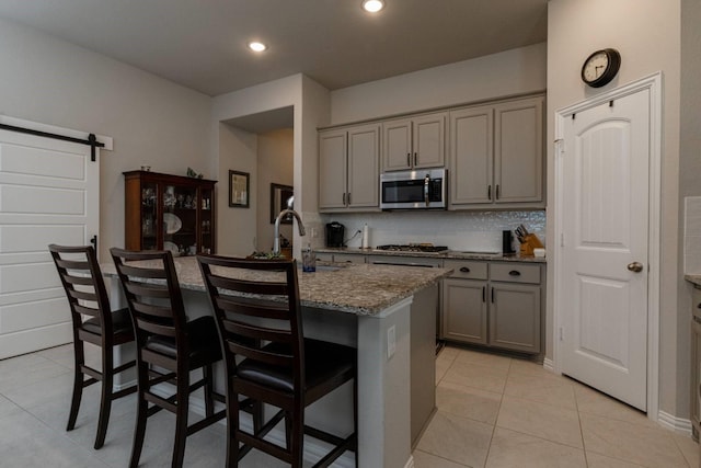 kitchen featuring a barn door, a kitchen island with sink, gray cabinetry, and stainless steel appliances