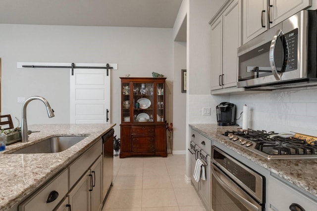 kitchen with light stone countertops, sink, a barn door, light tile patterned flooring, and appliances with stainless steel finishes