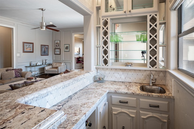 kitchen featuring sink, ceiling fan, ornamental molding, light stone counters, and white cabinetry