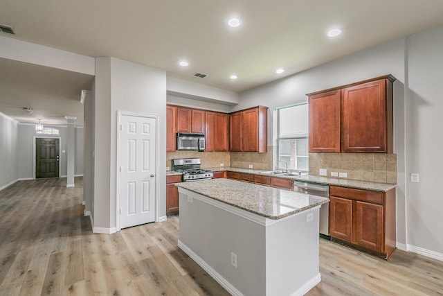 kitchen featuring a center island, light hardwood / wood-style flooring, stainless steel appliances, light stone countertops, and decorative backsplash