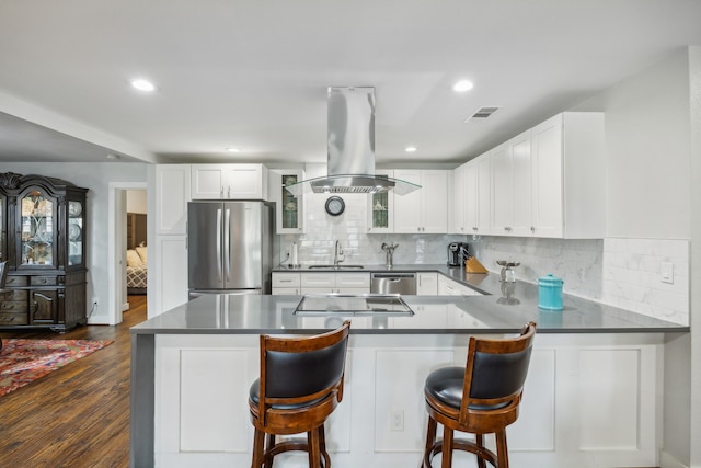 kitchen featuring a breakfast bar area, kitchen peninsula, island range hood, and stainless steel appliances