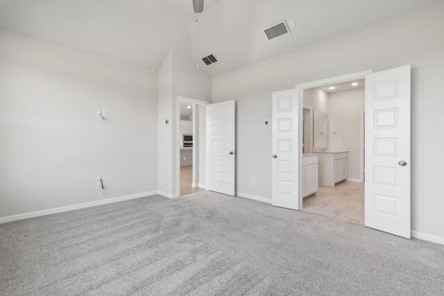 unfurnished bedroom featuring light carpet, high vaulted ceiling, and ensuite bath