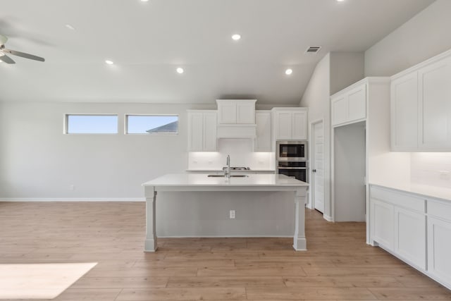 kitchen with built in microwave, sink, white cabinetry, stainless steel oven, and a kitchen island with sink