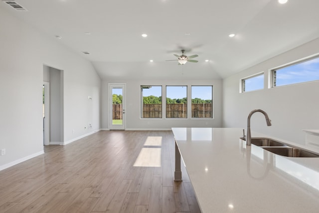 kitchen with light wood-type flooring, light stone counters, vaulted ceiling, ceiling fan, and sink