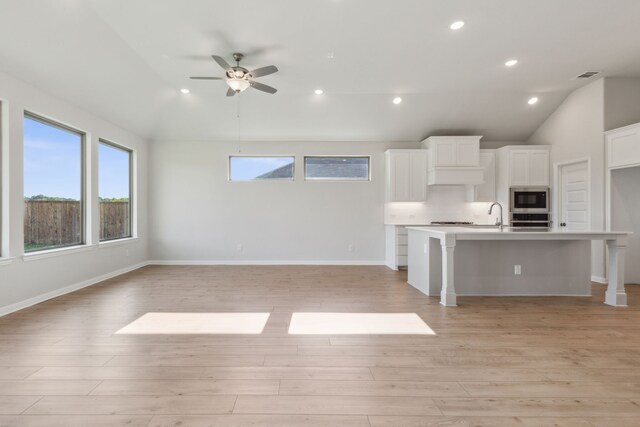 kitchen featuring appliances with stainless steel finishes, a breakfast bar area, a kitchen island with sink, white cabinets, and light wood-type flooring