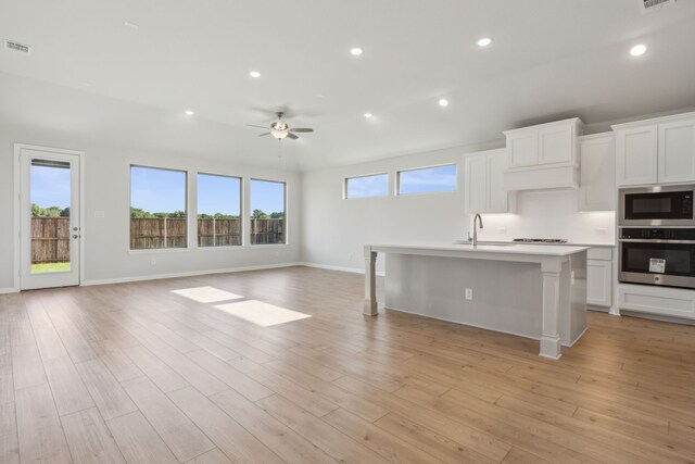 kitchen featuring built in microwave, ceiling fan, oven, an island with sink, and white cabinets