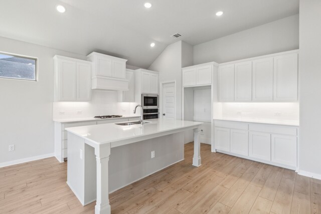 kitchen with backsplash, a kitchen island with sink, white cabinets, sink, and stainless steel appliances