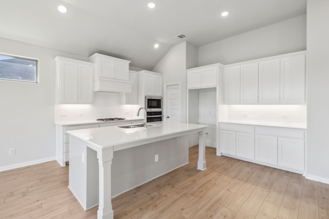 kitchen with sink, gas stovetop, white cabinets, a center island with sink, and built in microwave