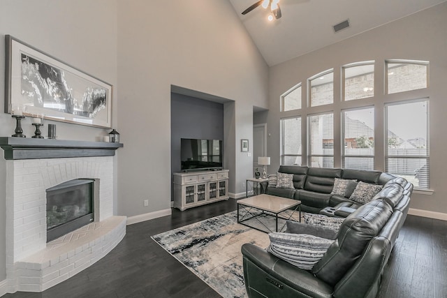 living room featuring high vaulted ceiling, dark hardwood / wood-style floors, a brick fireplace, and ceiling fan