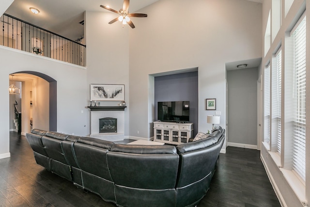 living room with a brick fireplace, dark hardwood / wood-style floors, ceiling fan, and a towering ceiling