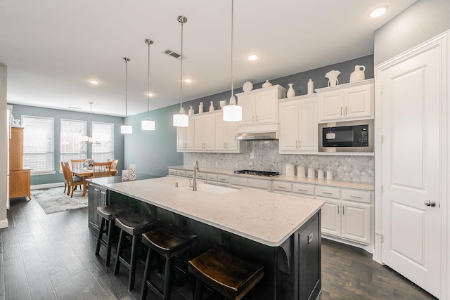 kitchen featuring a breakfast bar area, sink, an island with sink, and black microwave