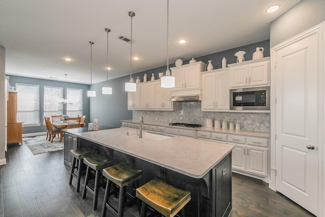 kitchen with built in microwave, white cabinets, and a kitchen island with sink