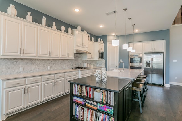 kitchen with appliances with stainless steel finishes, a center island with sink, white cabinetry, and a kitchen breakfast bar