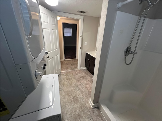 bathroom with walk in shower, vanity, stacked washer / dryer, and a textured ceiling