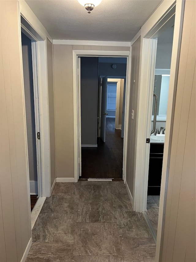 corridor with sink, a textured ceiling, and wooden walls