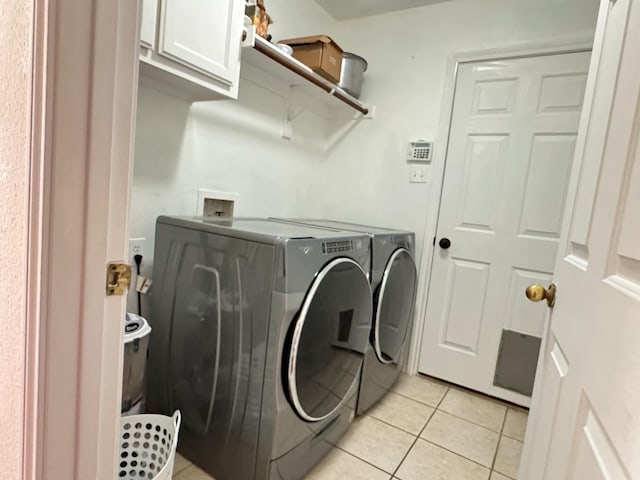 laundry area featuring washer and clothes dryer, light tile patterned floors, and cabinets