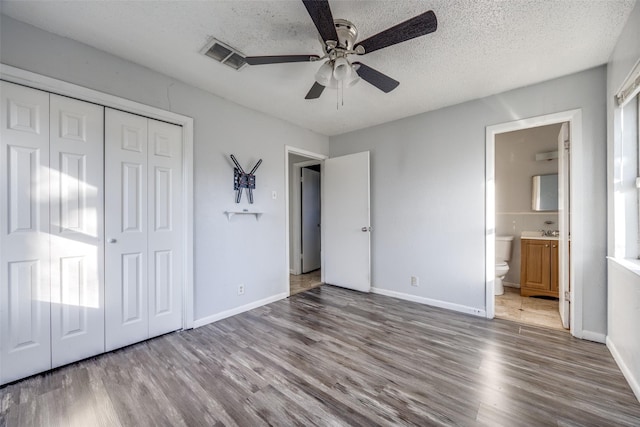 unfurnished bedroom featuring hardwood / wood-style flooring, ensuite bath, ceiling fan, a textured ceiling, and a closet