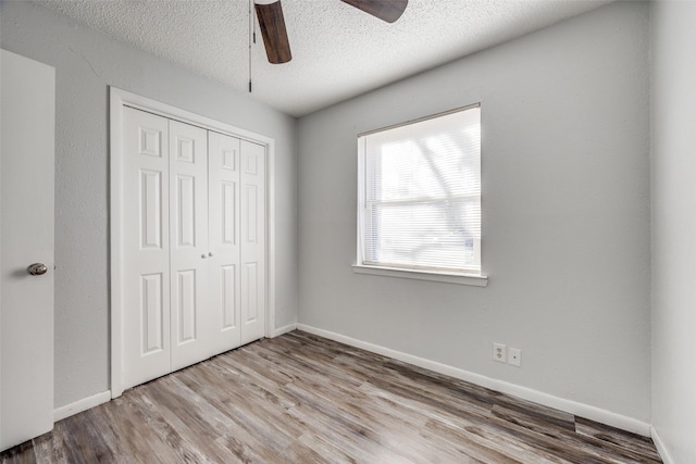 unfurnished bedroom with ceiling fan, wood-type flooring, a closet, and a textured ceiling