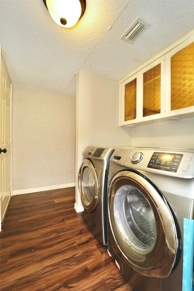 laundry room featuring cabinets, a textured ceiling, dark hardwood / wood-style floors, and washing machine and clothes dryer