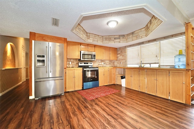 kitchen with appliances with stainless steel finishes, dark hardwood / wood-style flooring, backsplash, a textured ceiling, and a tray ceiling