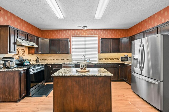 kitchen with dark brown cabinetry, a center island, light stone counters, a textured ceiling, and appliances with stainless steel finishes