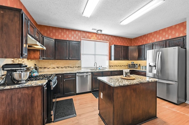 kitchen featuring sink, light stone countertops, dark brown cabinets, a kitchen island, and stainless steel appliances