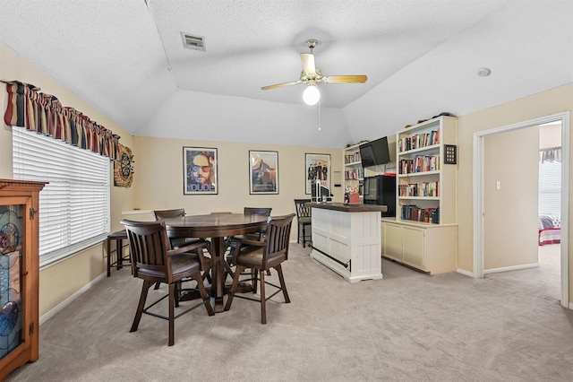 dining area with a textured ceiling, ceiling fan, light carpet, and vaulted ceiling