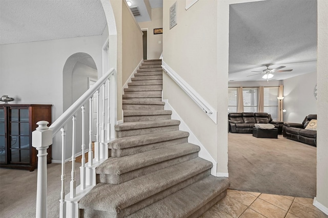 stairs with ceiling fan, carpet floors, and a textured ceiling