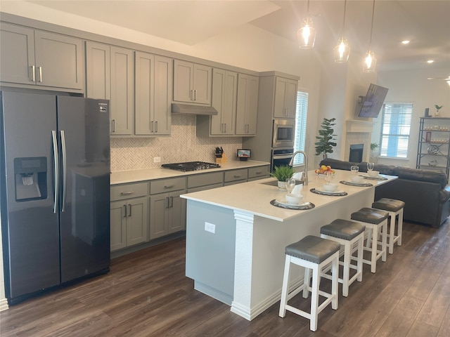 kitchen featuring backsplash, stainless steel appliances, a center island with sink, gray cabinets, and dark hardwood / wood-style floors