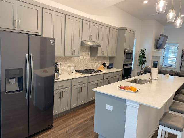 kitchen with a center island with sink, sink, gray cabinets, appliances with stainless steel finishes, and decorative light fixtures