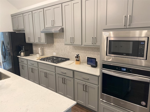 kitchen featuring decorative backsplash, light stone counters, stainless steel appliances, dark wood-type flooring, and gray cabinets