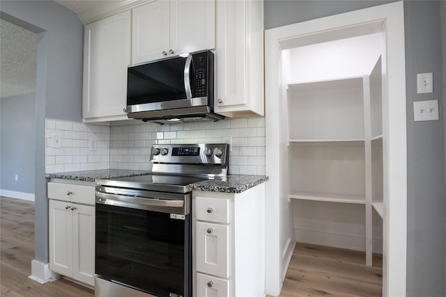 kitchen with stainless steel appliances, dark stone countertops, white cabinets, and decorative backsplash