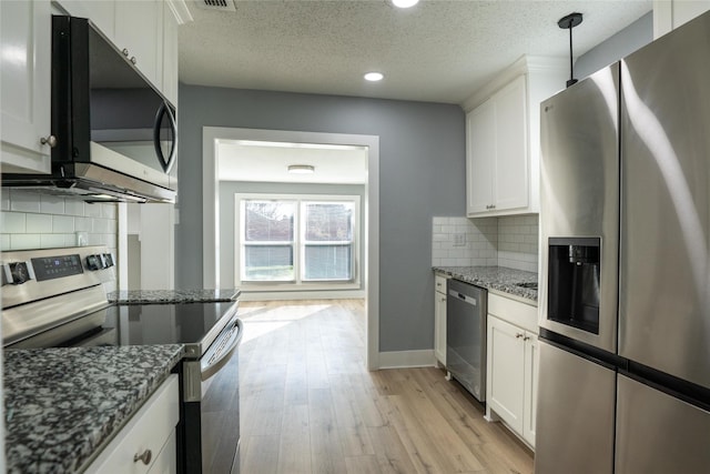 kitchen featuring white cabinetry, decorative light fixtures, stainless steel appliances, and dark stone countertops