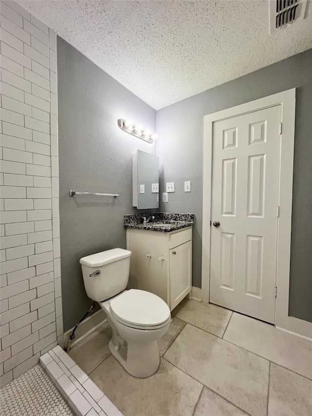 bathroom with tile patterned flooring, vanity, a textured ceiling, and toilet