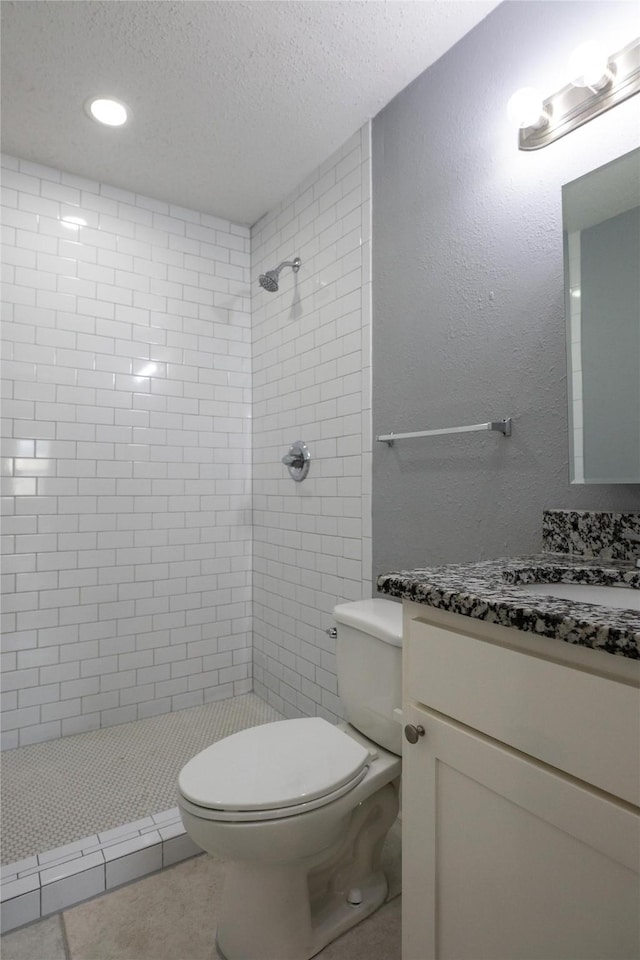 bathroom featuring tile patterned flooring, vanity, a tile shower, a textured ceiling, and toilet