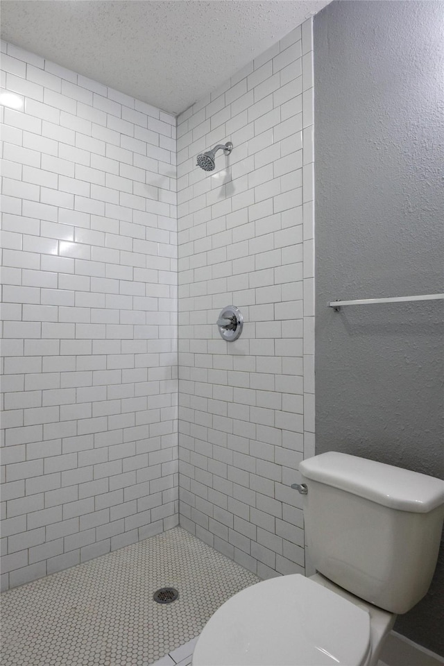 bathroom with a tile shower, toilet, and a textured ceiling