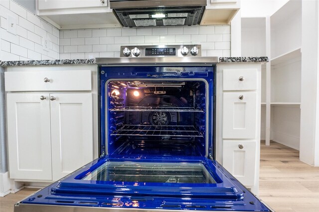 details with white cabinetry, backsplash, dark stone countertops, and light wood-type flooring