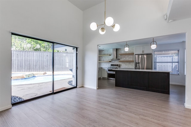 kitchen with pendant lighting, wall chimney range hood, hardwood / wood-style flooring, a notable chandelier, and stainless steel appliances