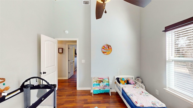 bedroom with ceiling fan, dark hardwood / wood-style floors, a high ceiling, and multiple windows