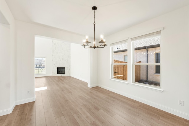 unfurnished dining area featuring light wood-type flooring, baseboards, a chandelier, and a fireplace