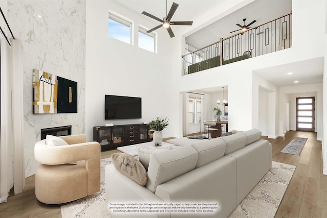 living room featuring wood finished floors, ceiling fan with notable chandelier, and a premium fireplace