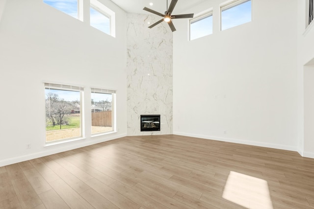 unfurnished living room with light wood-style flooring, baseboards, a ceiling fan, and a towering ceiling