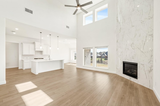 unfurnished living room featuring a ceiling fan, visible vents, a premium fireplace, light wood-style flooring, and a sink