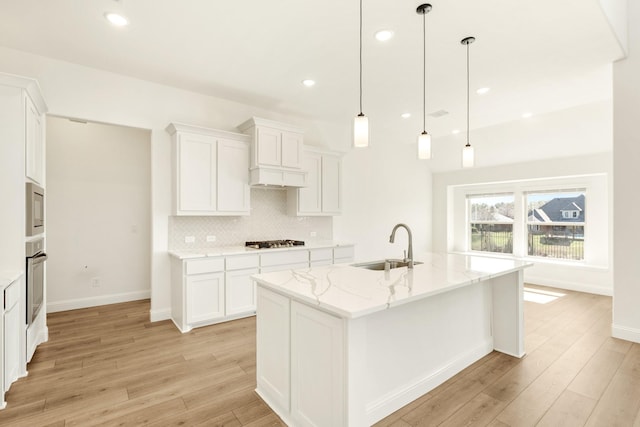 kitchen with gas cooktop, light wood finished floors, a sink, oven, and backsplash